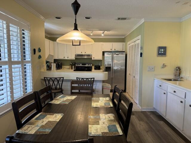 dining area with dark wood-style floors, visible vents, baseboards, and crown molding