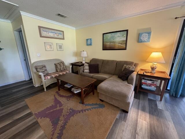 living room featuring a textured ceiling, ornamental molding, dark wood-style flooring, and visible vents