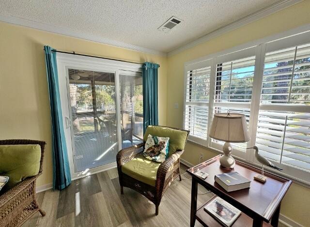 living area featuring visible vents, ornamental molding, a textured ceiling, wood finished floors, and baseboards