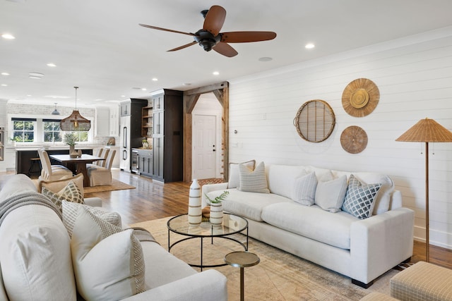 living room with ceiling fan, light wood-type flooring, and wood walls