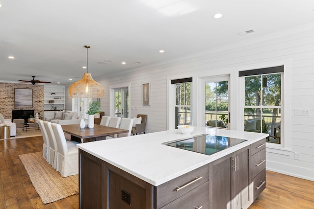 kitchen with ceiling fan, black electric stovetop, a fireplace, a center island, and light wood-type flooring