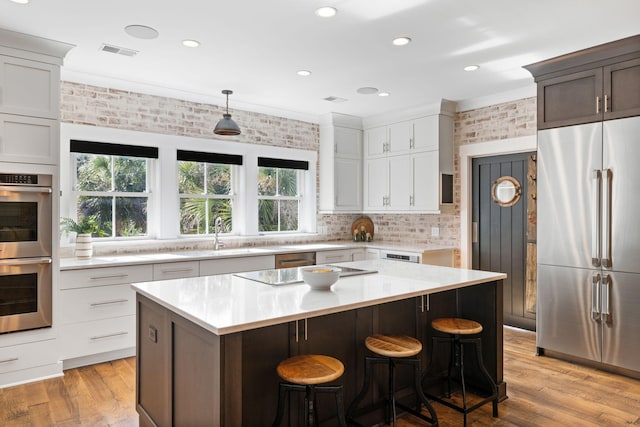 kitchen with appliances with stainless steel finishes, a kitchen island, light wood-type flooring, crown molding, and sink