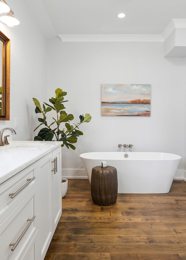 bathroom with a tub to relax in, hardwood / wood-style floors, vanity, and crown molding