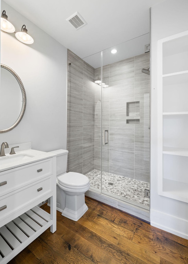 bathroom with wood-type flooring, a shower with door, vanity, and toilet