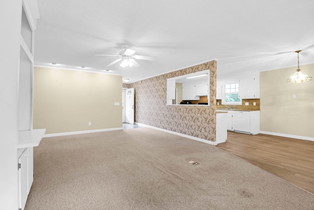 unfurnished living room featuring crown molding, sink, ceiling fan with notable chandelier, and light wood-type flooring