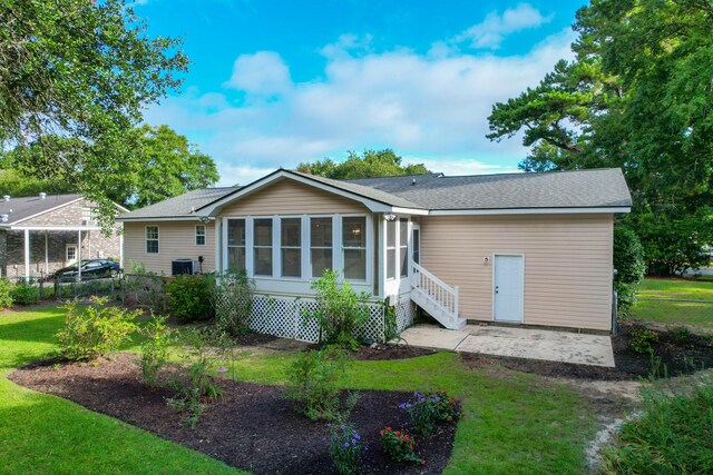 rear view of house with a sunroom, a lawn, and central AC