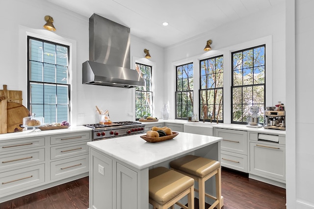 kitchen with wall chimney range hood, sink, a kitchen island, a breakfast bar, and dark hardwood / wood-style floors