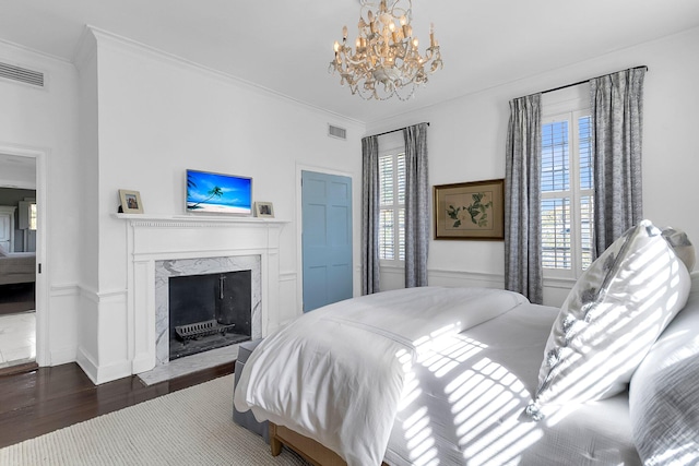 bedroom with a premium fireplace, crown molding, dark wood-type flooring, and an inviting chandelier