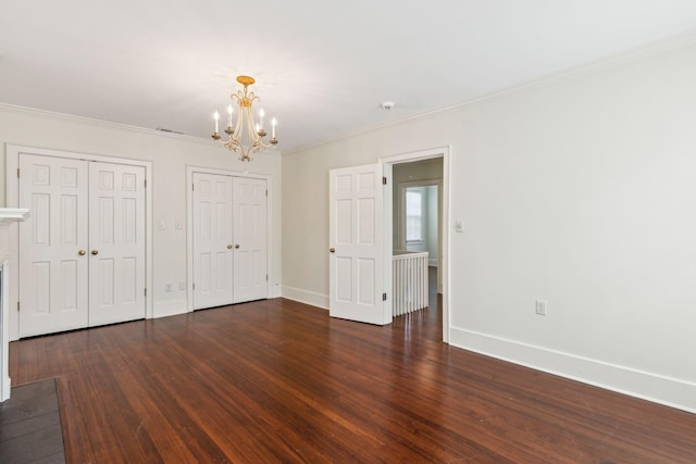 unfurnished bedroom featuring multiple closets, dark wood-type flooring, crown molding, and a chandelier