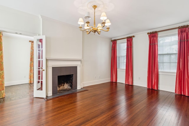 unfurnished living room featuring dark hardwood / wood-style floors, a wealth of natural light, a tiled fireplace, and an inviting chandelier