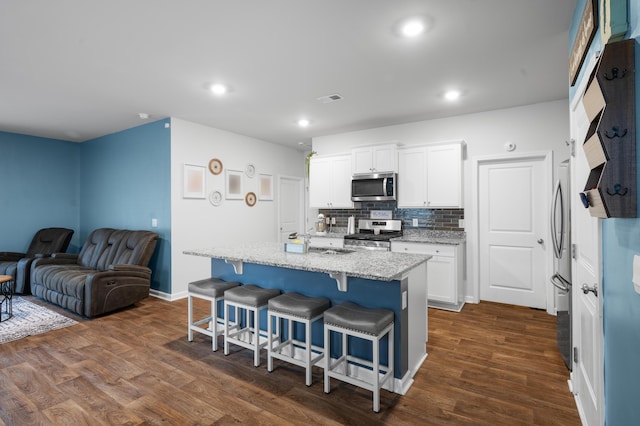 kitchen with white cabinetry, dark wood-type flooring, a kitchen island with sink, and appliances with stainless steel finishes