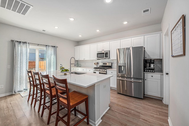 kitchen featuring a kitchen island with sink, appliances with stainless steel finishes, a breakfast bar, sink, and white cabinetry