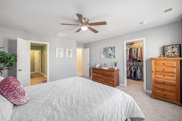 bedroom featuring a walk in closet, light colored carpet, ceiling fan, and a closet