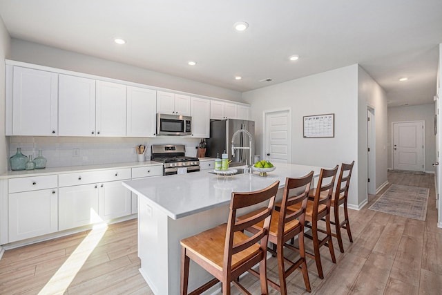 kitchen featuring white cabinetry, a center island with sink, appliances with stainless steel finishes, a kitchen bar, and light hardwood / wood-style flooring