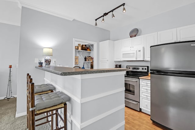 kitchen featuring white cabinets, a breakfast bar area, light wood-type flooring, kitchen peninsula, and stainless steel appliances