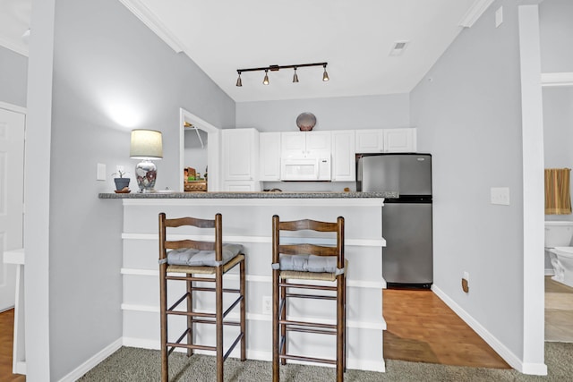 kitchen with kitchen peninsula, rail lighting, a breakfast bar, white cabinetry, and stainless steel refrigerator