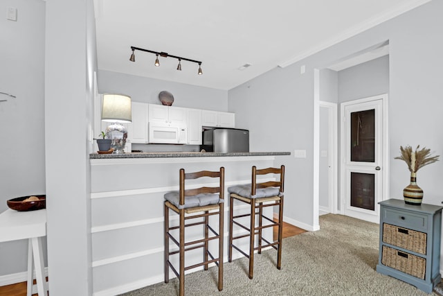 kitchen featuring light carpet, white cabinetry, stainless steel refrigerator, and a breakfast bar area