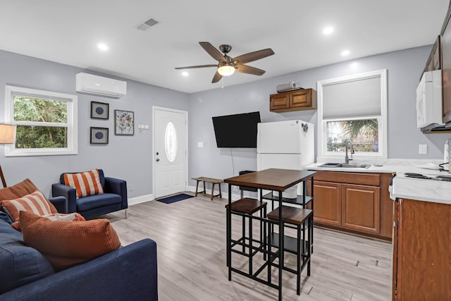 kitchen with white appliances, a wall mounted AC, light wood-type flooring, ceiling fan, and sink