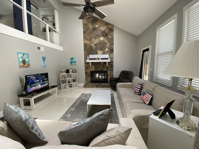 tiled living room with a healthy amount of sunlight, ceiling fan, a stone fireplace, and high vaulted ceiling