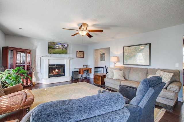 living room featuring dark hardwood / wood-style flooring, ceiling fan, and a textured ceiling