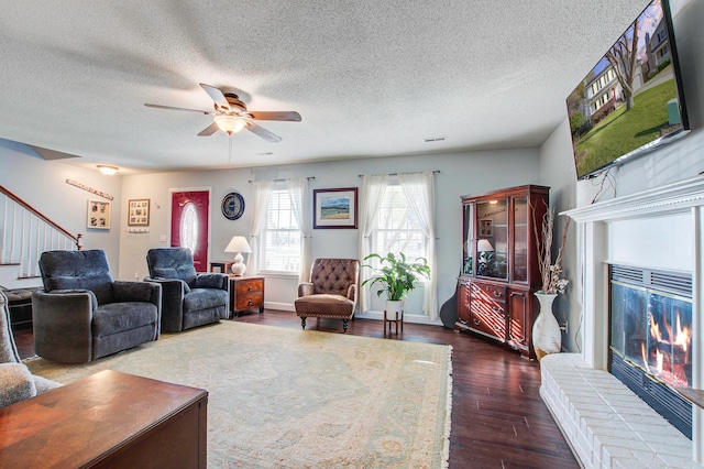 living room with dark wood-type flooring, ceiling fan, a textured ceiling, and a fireplace