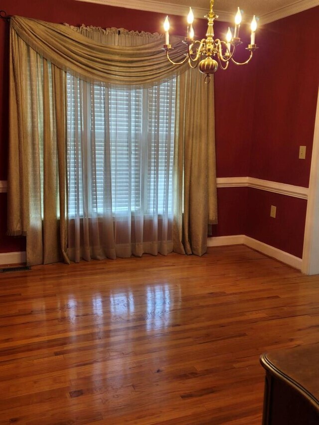 spare room featuring wood-type flooring, a notable chandelier, and crown molding