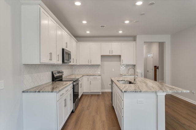 kitchen with light stone counters, wood finished floors, a sink, white cabinets, and appliances with stainless steel finishes