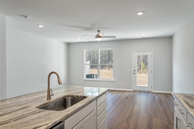 kitchen with a sink, light stone counters, recessed lighting, white cabinetry, and dark wood-style flooring