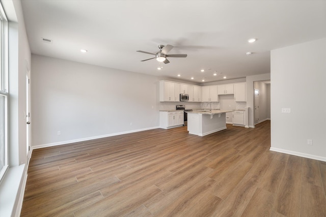 unfurnished living room with light wood-style flooring, a ceiling fan, a sink, recessed lighting, and baseboards