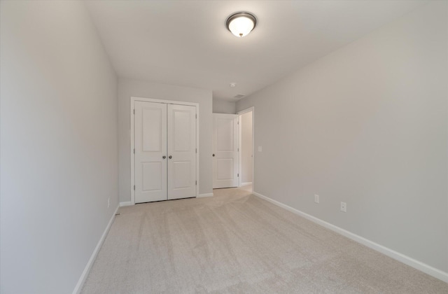 unfurnished bedroom with a closet, light colored carpet, and baseboards