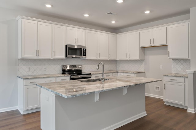 kitchen with dark wood finished floors, light stone counters, white cabinets, stainless steel appliances, and a sink