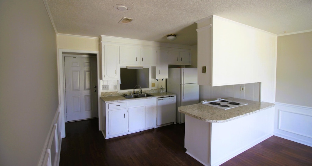 kitchen featuring a peninsula, white appliances, a sink, and dark wood finished floors