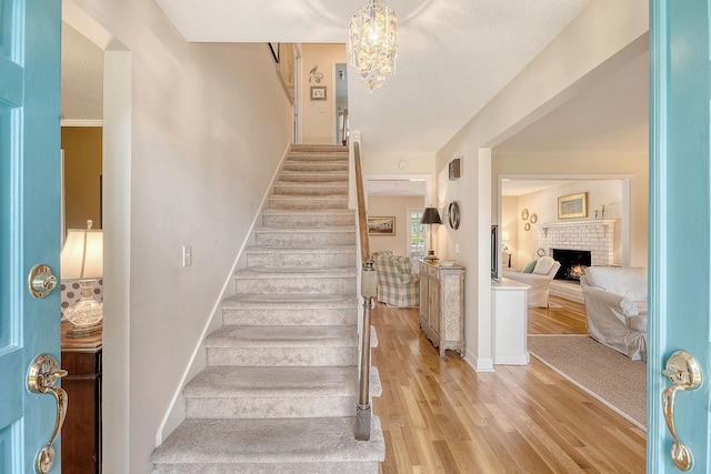 staircase with wood finished floors, a brick fireplace, a chandelier, and baseboards