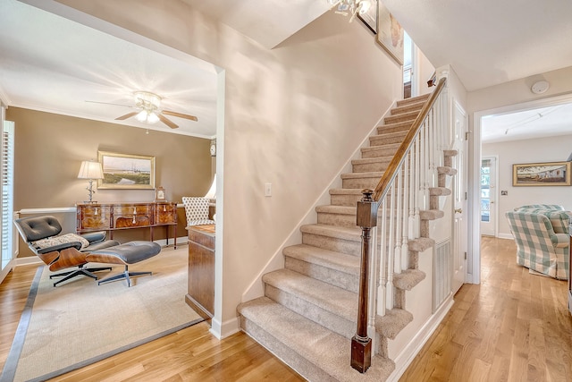 staircase with wood finished floors, ceiling fan, baseboards, and ornamental molding