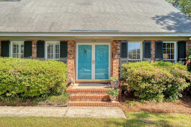 property entrance with a shingled roof, brick siding, and french doors