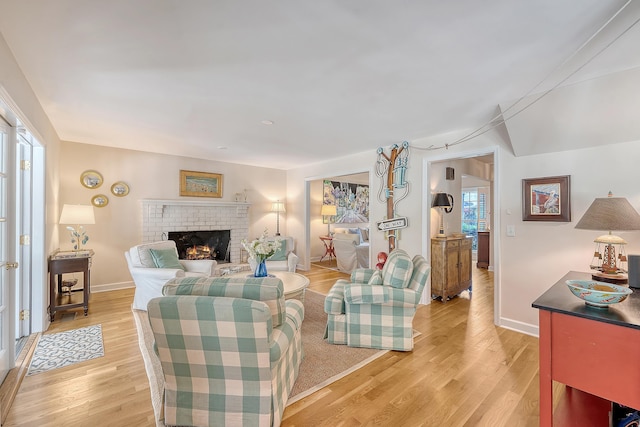 living area with light wood-style floors, a brick fireplace, and baseboards