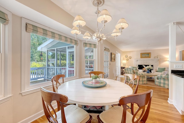 dining room with light wood-style floors, a fireplace, a chandelier, and baseboards