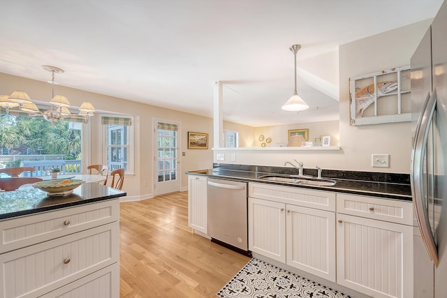 kitchen featuring appliances with stainless steel finishes, a sink, light wood-style floors, decorative light fixtures, and a chandelier