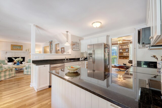 kitchen with a peninsula, appliances with stainless steel finishes, white cabinets, and light wood-style flooring