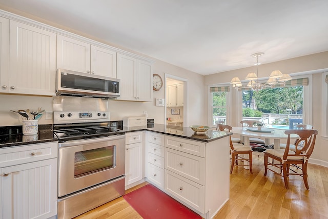 kitchen featuring stainless steel appliances, a peninsula, light wood-type flooring, a chandelier, and white cabinets