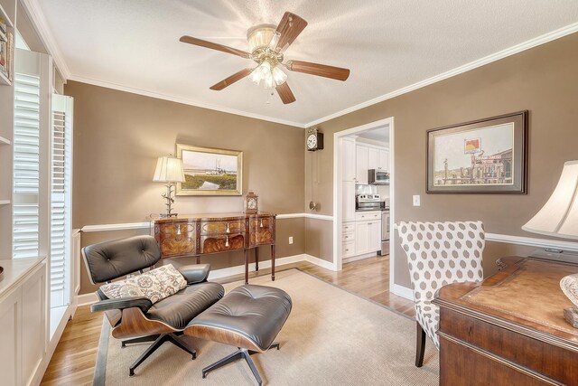 living area with light wood-type flooring, a ceiling fan, crown molding, and baseboards
