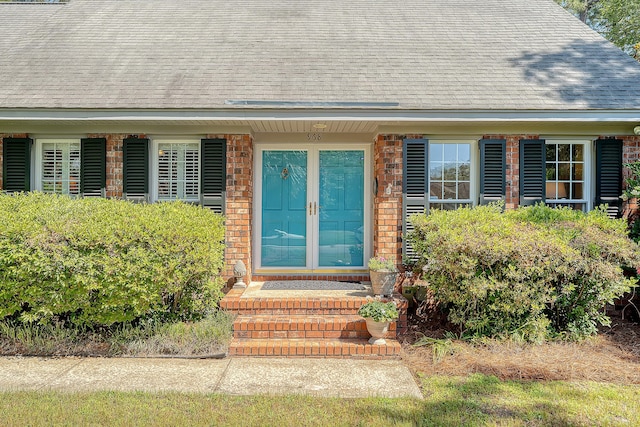 property entrance featuring roof with shingles and brick siding