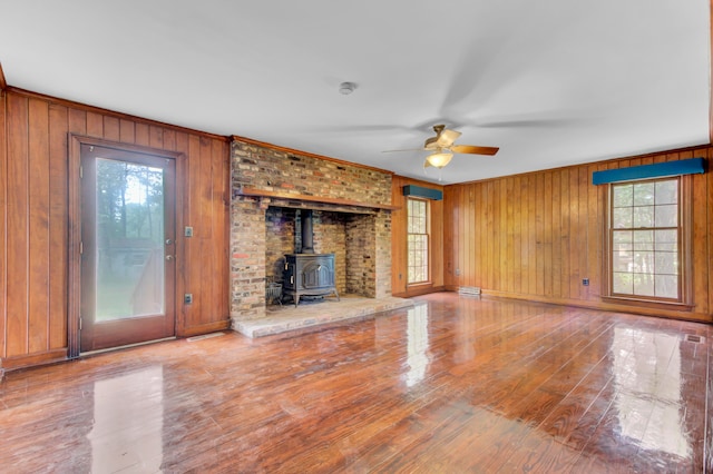 unfurnished living room featuring hardwood / wood-style floors, wood walls, a wood stove, and ceiling fan