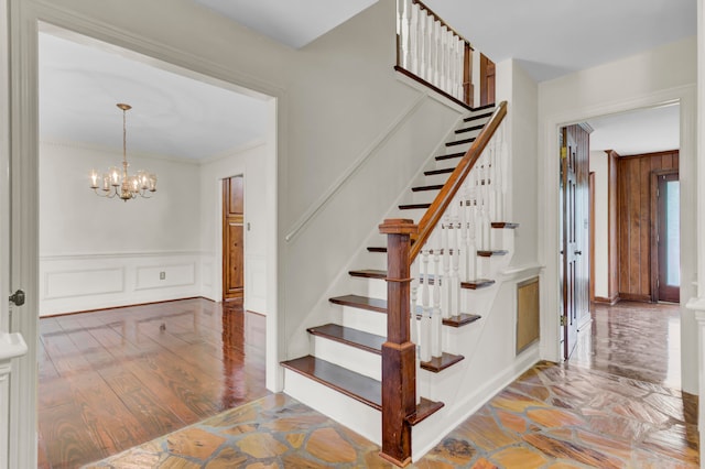 stairway with a notable chandelier, hardwood / wood-style flooring, and ornamental molding