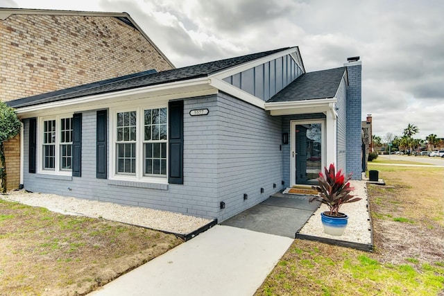 view of front of home with roof with shingles, brick siding, and board and batten siding