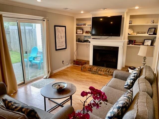 living room with built in features, light wood-type flooring, a brick fireplace, and crown molding