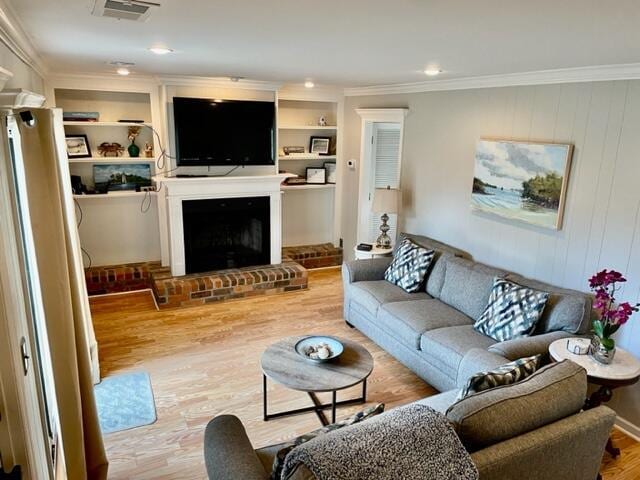 living room featuring a fireplace, light wood-type flooring, built in features, and crown molding