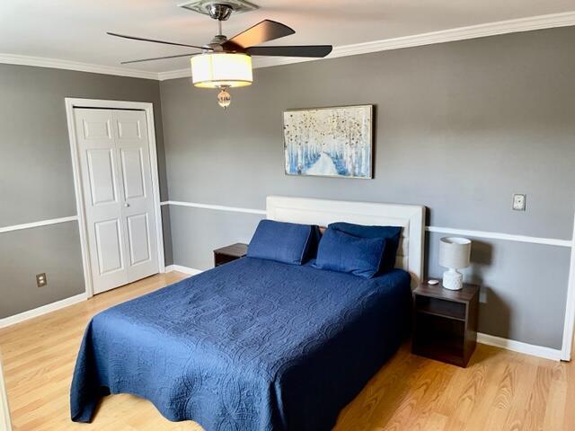 bedroom with crown molding, ceiling fan, a closet, and wood-type flooring