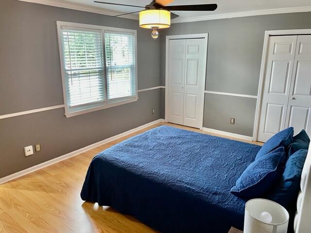 bedroom with multiple closets, hardwood / wood-style flooring, ceiling fan, and crown molding