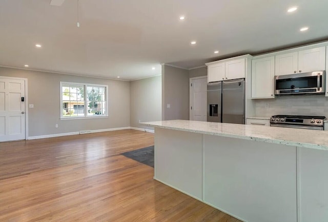 kitchen with white cabinets, light wood-type flooring, light stone countertops, and appliances with stainless steel finishes